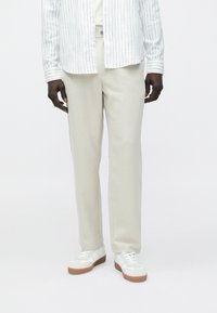 Calças bege claro feitas de tecido macio, com corte reto e textura sutil. Combinadas com ténis brancos com solas de borracha.