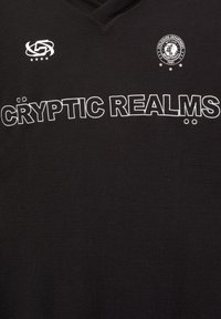 Černá tkanina s bílým obrysem textu "CRYPTO REALMS" a dvěma malými logy nad ním, jedno kruhové s textem a jedno abstraktní se hvězdami.