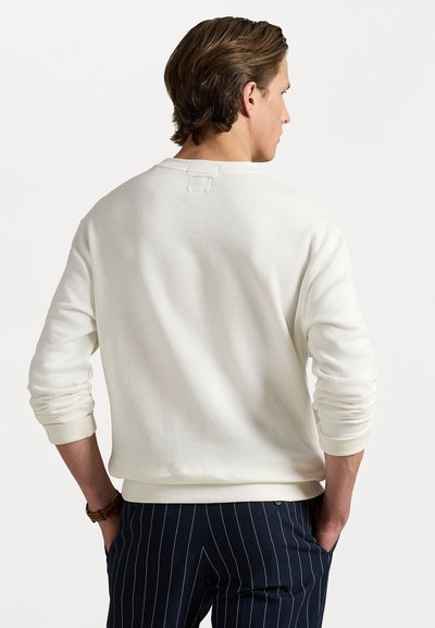 Sweatshirt alb cu mâneci lungi, cu mansete ribelate și o croială boxy. Țesătură texturată și un detaliu mic cu etichetă la spate. Asortat cu pantaloni cu dungi.