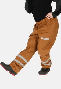 Bruine waterdichte broek met reflecterende strepen, elastische tailleband en een gladde afwerking. Draagt over donkere schoenen, met een aansluitend ontwerp.