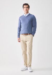 Jasnoniebieski sweter w serek, koszula z kołnierzykiem, beżowe chinosy, brązowy pasek, białe sneakersy. Prosty wzór, gładka tekstura, brak widocznych wzorów.