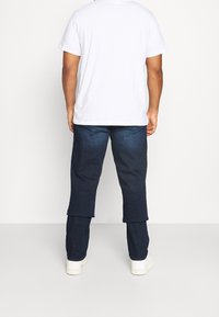 Pantalones de mezclilla azul oscuro con un corte relajado, que presentan una textura suave y un diseño sencillo. Combinados con una camiseta blanca lisa y zapatos blancos.