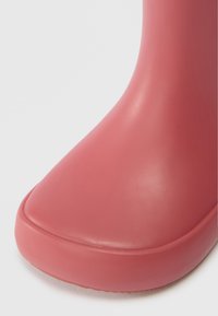 Κοντινό πλάνο μιας ματ ροζ καουτσούκ μπότας με στρογγυλεμένη μύτη και λεία επιφάνεια σε λευκό φόντο.