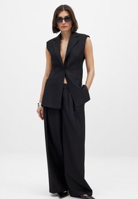 Must mustriga vest, millel on sügav V-kaelus ja kraed, koos laia säärega pükstega. Sile kangas, minimalistlik disain ja nähtavad mustrid puuduvad.