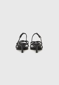Black heeled sandals with a minimalist design, featuring slender straps and a block heel. Smooth texture with a polished finish.