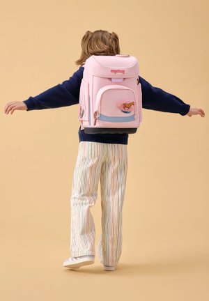 Child with striped pants and navy sweater wearing pink school backpack with horse design, arms extended against plain beige background.