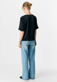 Schwarzes Kurzarm-Oberteil mit lockerer Passform, kombiniert mit hellblauen, weiten Jeans. Der Stoff wirkt glatt und das Outfit ist lässig.