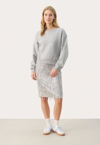 Grijze sweatshirt met een ronde hals, gecombineerd met een zilveren franjesrok. Witte sneakers en lichtgekleurde sokken maken de outfit compleet.