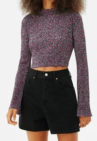 Top court à manches longues en tissu noir avec un petit motif floral rose et vert. Associé à un short en denim noir taille haute.