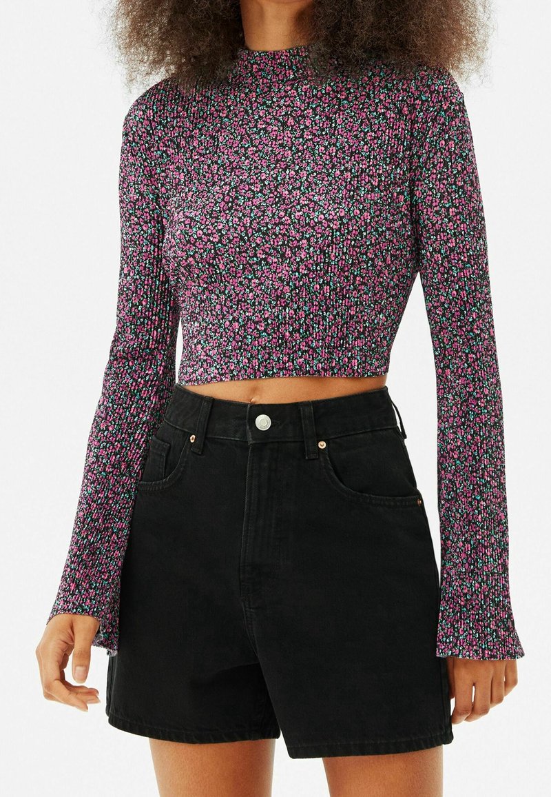 Top court à manches longues en tissu noir avec un petit motif floral rose et vert. Associé à un short en denim noir taille haute.