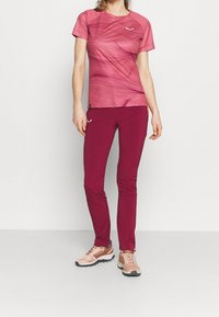 T-shirt de sport rose à rayures horizontales, associé à un pantalon fuselé couleur bordeaux. Comprend des baskets texturées de couleur claire avec des semelles foncées.