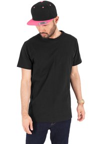 Černé tričko s krátkým rukávem vyrobené z bavlny, doplněné černou a růžovou kšiltovkou snapback s plochým kšiltem a kontrastními akcenty.