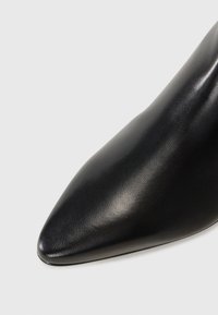 Chaussure à talon haut en cuir noir avec un bout pointu et une texture lisse, mettant en avant un design élégant et un style minimaliste.