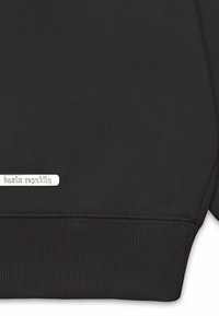 Sort sweatshirt med ribbede mansjetter og kant, med et sølvmærke prægede med "bazix republiq" nær bunden. Glat tekstur.