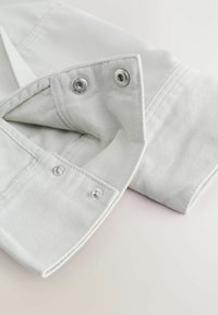 Manșon de jachetă din denim alb cu două capse metalice închise și două deschise, evidențiind detalii cu dublă cusătură.