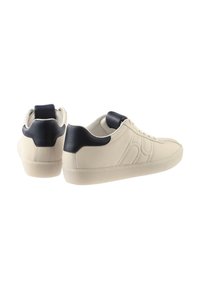 Leather sneakers with a cream body and navy accents. Features include a rounded toe, lace-up front, and textured details on the sides.
