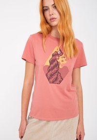 Korte mouwen roze T-shirt van katoen, met een afbeelding van het profiel van een vrouw in bruin en goud binnen een diamantvorm.