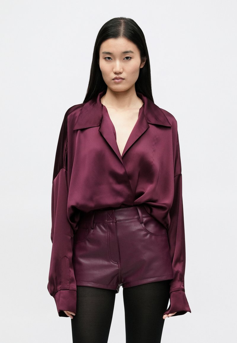 Bordo spalvos satino palaidinė su iškirptu atlapu, laisvo kirpimo ir ilgomis rankovėmis; derinama su aukšto juosmens odai panašiomis šortais.