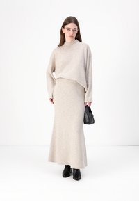 Beige Strickpullover und langer Rock, mit einem lockeren Schnitt, Rippdetails und kombiniert mit einer schwarzen Handtasche und Ankle Boots.