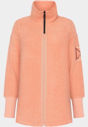 Veste en polaire couleur pêche avec un col montant, fermeture éclair et manches longues ; présente un tissu texturé et un accent en forme de triangle distinctif sur la manche.