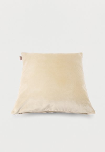 Coussin carré beige avec une texture de tissu doux posé à plat sur une surface blanche.