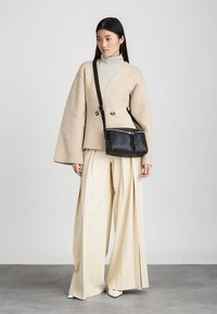 Blazer oversize in misto lana beige, borsa a tracolla nera con zip, pantaloni a gamba larga color crema e dolcevita a righe. Texture lisce, design moderno.