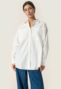 Hvid bomulds skjorte med knapper og lange ærmer, to forlommer, en klassisk krave og en afslappet pasform, parret med blå vide jeans.