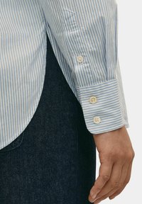 Gestreepte button-up shirt in lichtblauw en wit, met lange mouwen met knopen op de manchetten en een gebogen zoom, gecombineerd met donkere denim.
