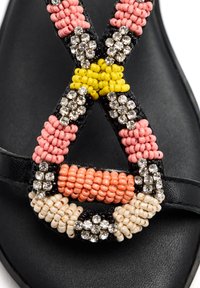 Sandalia negra con una correa decorativa de cuentas que presenta cuentas rosas, amarillas y coral, intercaladas con rhinestones plateados para un detalle adicional.