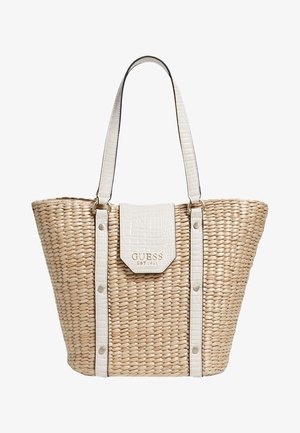 Beżowa pleciona torba typu tote z białymi paskami i klapą z ekoskóry, z złotym logo "GUESS EST 1981" na przedniej klapie.