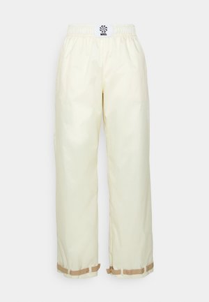 Krämfärgade joggerbyxor med elastisk midja, avsmalnande ben och beige detaljer vid fållen. Har en logotypapplikation på baksidan.