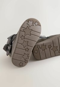 Szare podeszwy butów z wzorem gwiazdy, teksturowane dla lepszego uchwytu. Projekt zawiera poziome linie oraz wypukłe gwiazdy o różnych rozmiarach.