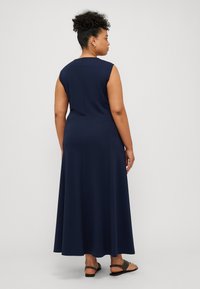 Mörkblå ärmlös klänning i en flytande design, med en slät textur och knälång fåll. I kombination med svarta platta sandaler.