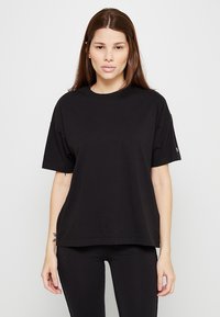 Černé oversized tričko vyrobené z bavlny, s kulatým výstřihem a krátkými rukávy. Hladká textura s minimalistickým designem a bez vzorů.
