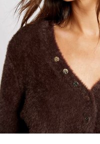 Bruine, pluizige cardigan met een V-hals, drie decoratieve knopen in verschillende kleuren en een zachte, gestructureerde stof.