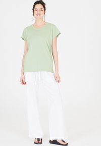 Ljusgrön bomullströja med korta ärmar, matchad med lösa vita linbyxor och svarta flip-flops. Enkel, avslappnad passform och design.