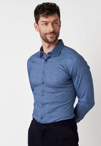 Langarmige, knoopsluiting shirt in een gestructureerde donkerblauwe stof, met een scherpe kraag en contrasterende knopen, gedragen in een donkere broek.