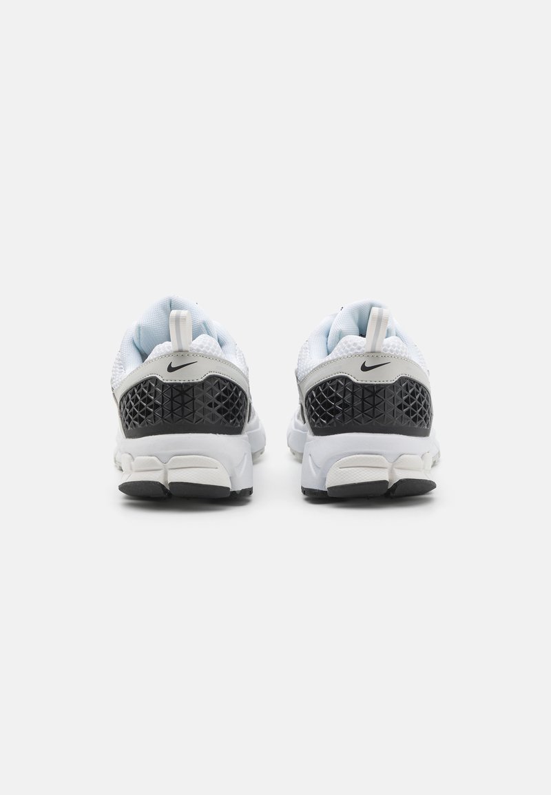 Baskets Nike avec une tige en mesh blanc, un talon texturé noir et une semelle en caoutchouc grise. Comprend un onglet en boucle et des accents de motifs intrigants.