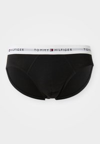 Sorte herretrusser med hvid elastik i taljen, der har Tommy Hilfiger-logo og flagmønster, vist fladt på en hvid baggrund.