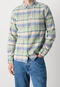 Lekka koszula w kratę z zielonymi, niebieskimi i różowymi paskami na kremowym tle. Długie rękawy, zapinany kołnierzyk i luźny krój.