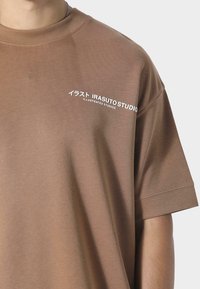 Lysebrun oversized t-shirt lavet af blødt stof, med rund hals og korte ærmer, prydet med hvid tekst trykt på forsiden.