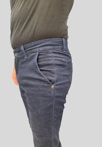 Pantaloni in denim blu scuro con vestibilità slim, dotati di un singolo bottone dorato e tasche frontali inclinate. Cuciture visibili e tessuto texturizzato.