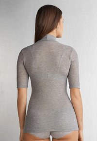 Šedý žebrovaný top s krátkým rukávem, který má vysoký límec a přiléhavý střih. Textura vypadá jemně s mírným leskem.