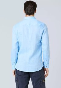 Camicia di lino azzurro chiaro con maniche lunghe, polsini con bottoni, colletto alla francese e orlo dritto, che mostra una trama liscia sul retro.