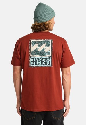 Roestkleurig katoen t-shirt met een grote grafische print op de achterkant, voorzien van blauwe golfpatronen en de tekst "BILLABONG" in een sierlijk ontwerp. Korte mouwen.