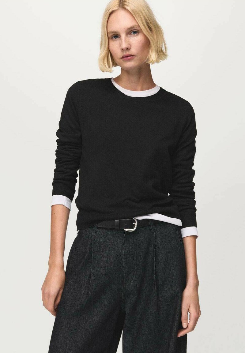 Schwarzer Pullover mit weißem Rundhalsausschnitt und Bündchen, getragen zu dunkler, hochtaillierter Hose mit Gürtel und silberner Schnalle.