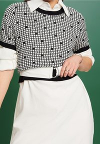Suéter corto a rayas en blanco y negro con mangas cortas, combinado con un vestido blanco y un cinturón negro con una hebilla redonda.