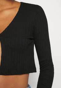 Svart ribbad stickad crop-top med långa ärmar, med en djup V-ringning och en figurnära silhuett, som visar en texturerad tyg.