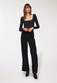 Body nero con scollatura quadrata e maniche lunghe, caratterizzato da un motivo a pois. Abbinato a pantaloni neri a vita alta e stivali con tacco.
