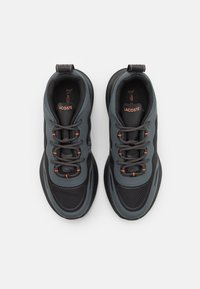 Baskets Lacoste avec une tige en mesh gris foncé, des accents gris et orange contrastants, un bout arrondi, et un système de laçage intégré.